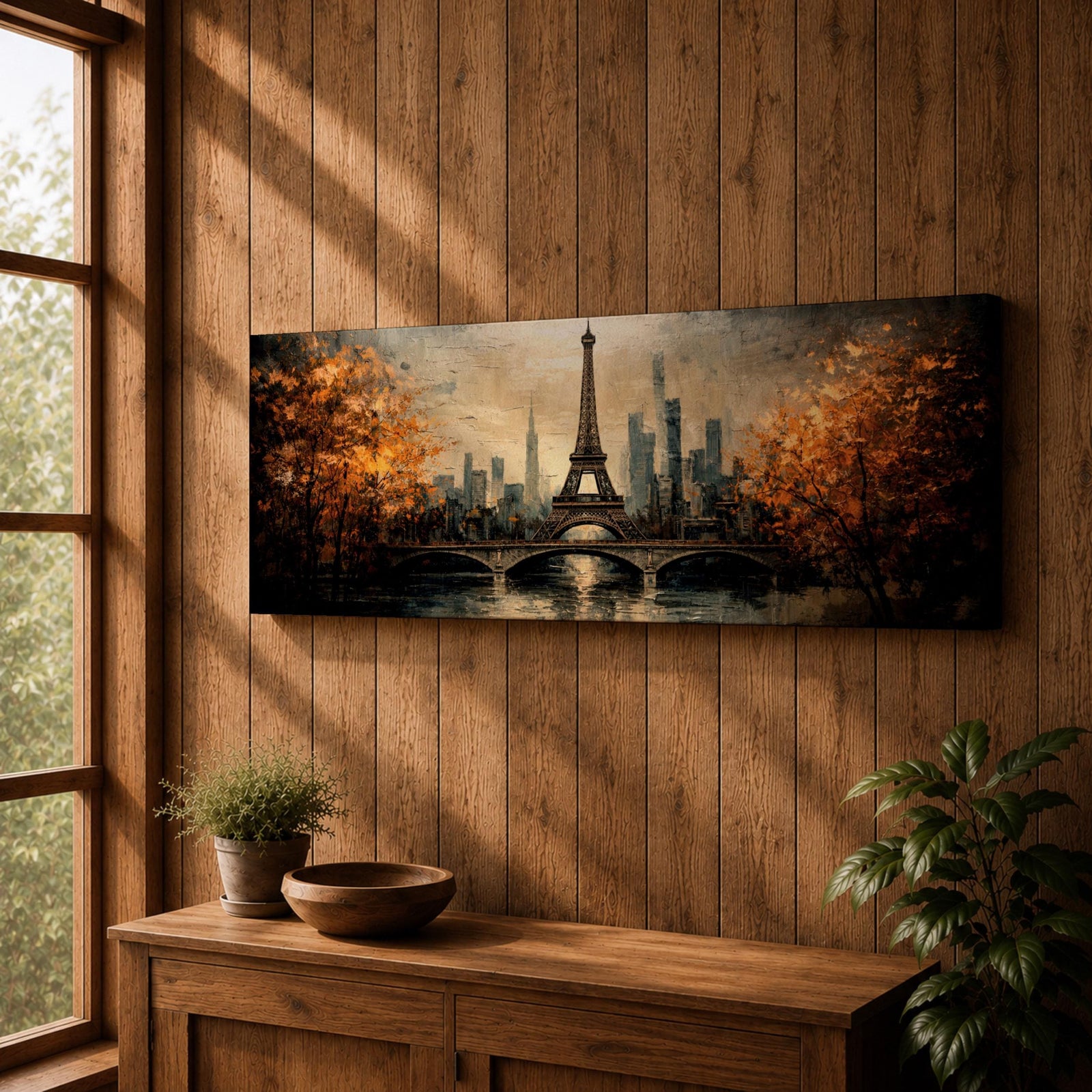 A long narrow panoramic painting depicts the Eiffel Tower rising above a river with an arched bridge in the foreground, surrounded by autumn trees and a distant city skyline, rendered in textured brushstrokes with warm golden tones and soft reflections that create depth and a romantic atmospheric cityscape.