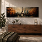 A long narrow panoramic painting depicts the Eiffel Tower rising above a river with an arched bridge in the foreground, surrounded by autumn trees and a distant city skyline, rendered in textured brushstrokes with warm golden tones and soft reflections that create depth and a romantic atmospheric cityscape.