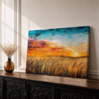A framed canvas painting depicting a wheat field at sunset with golden stalks swaying under a vibrant sky blending orange, yellow, and blue hues. The artwork captures a rustic farmhouse landscape scene with textured brushstrokes emphasizing natural elements and an expansive horizon.