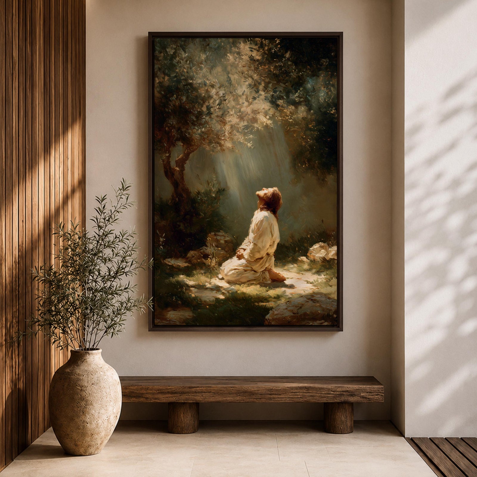 Framed artwork of Jesus praying in the Garden of Gethsemane, kneeling beneath a tree as soft rays of light shine down from above. Set in a modern living room, the canvas rests on a wooden console beside plants and neutral decor.
