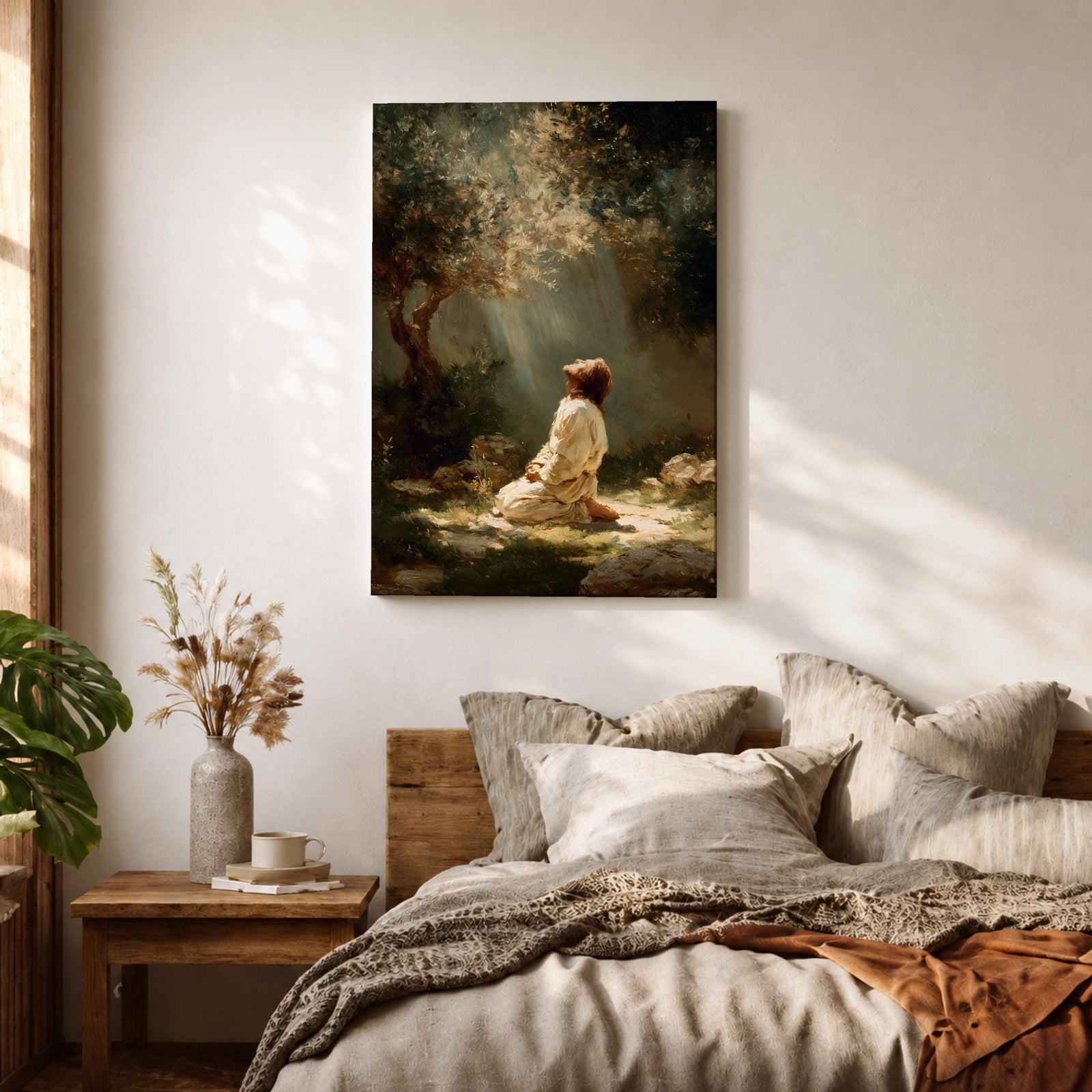 Framed artwork of Jesus praying in the Garden of Gethsemane, kneeling beneath a tree as soft rays of light shine down from above. Set in a modern living room, the canvas rests on a wooden console beside plants and neutral decor.