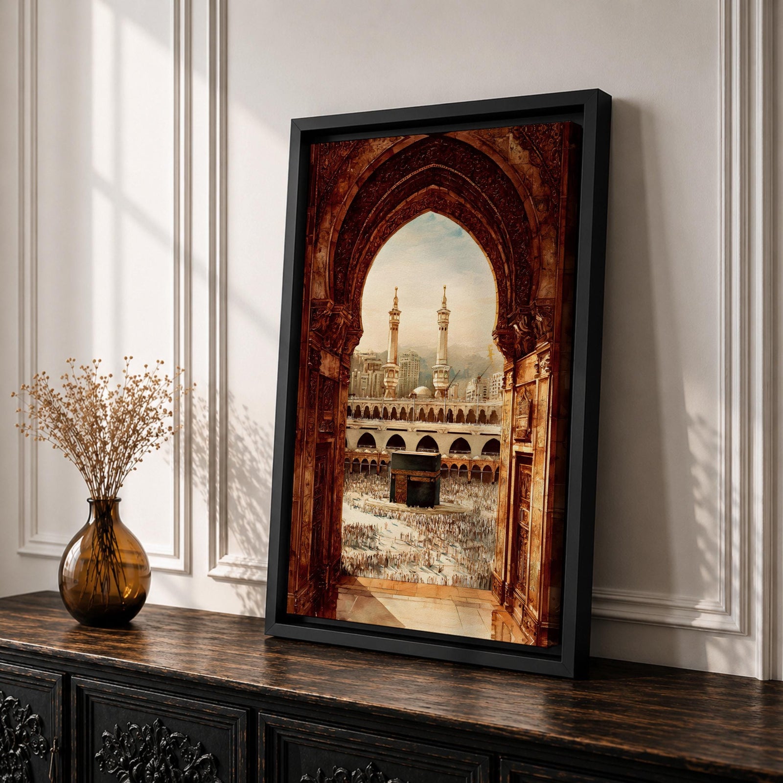 Artwork showing the Kaaba in Mecca viewed through an ornate Islamic archway with intricate carved stone details, overlooking the Masjid al Haram courtyard filled with pilgrims and surrounded by minarets and mosque architecture under warm sunlight.