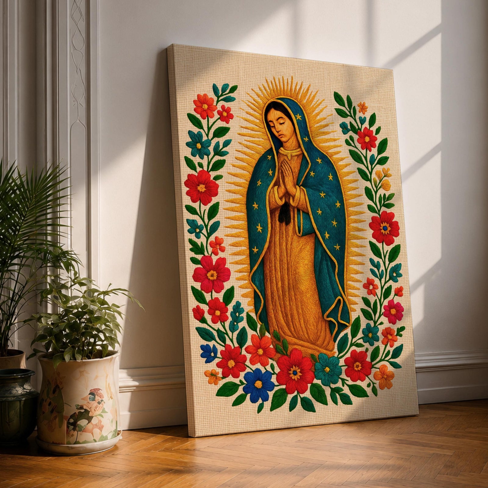 A framed stitched style art print depicting Our Lady of Guadalupe with hands clasped in prayer, surrounded by a radiant golden halo and vibrant floral embroidery in red, blue, and green. The image captures the traditional Mexican Catholic iconography with intricate textile detail and a serene expression.