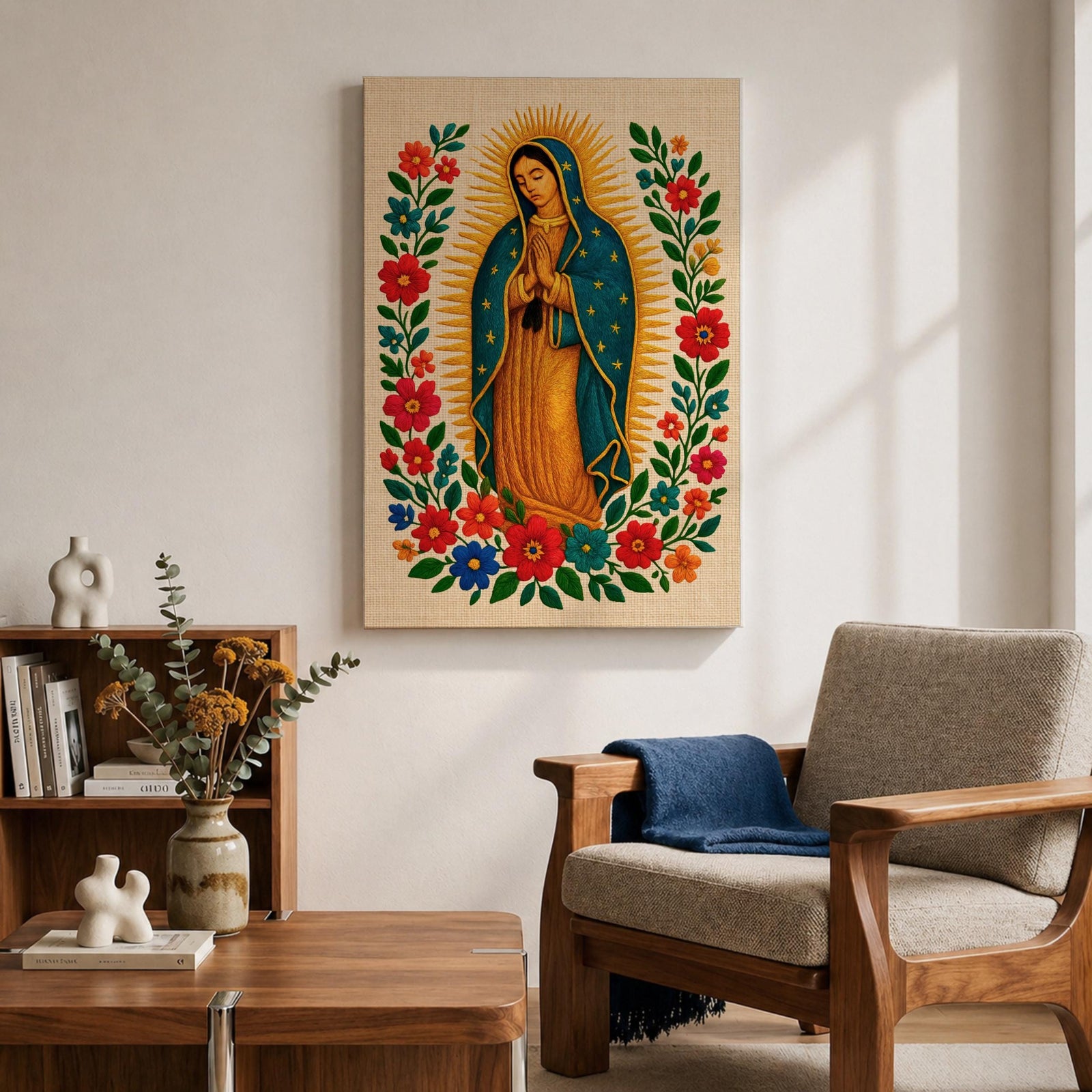 A framed stitched style art print depicting Our Lady of Guadalupe with hands clasped in prayer, surrounded by a radiant golden halo and vibrant floral embroidery in red, blue, and green. The image captures the traditional Mexican Catholic iconography with intricate textile detail and a serene expression.