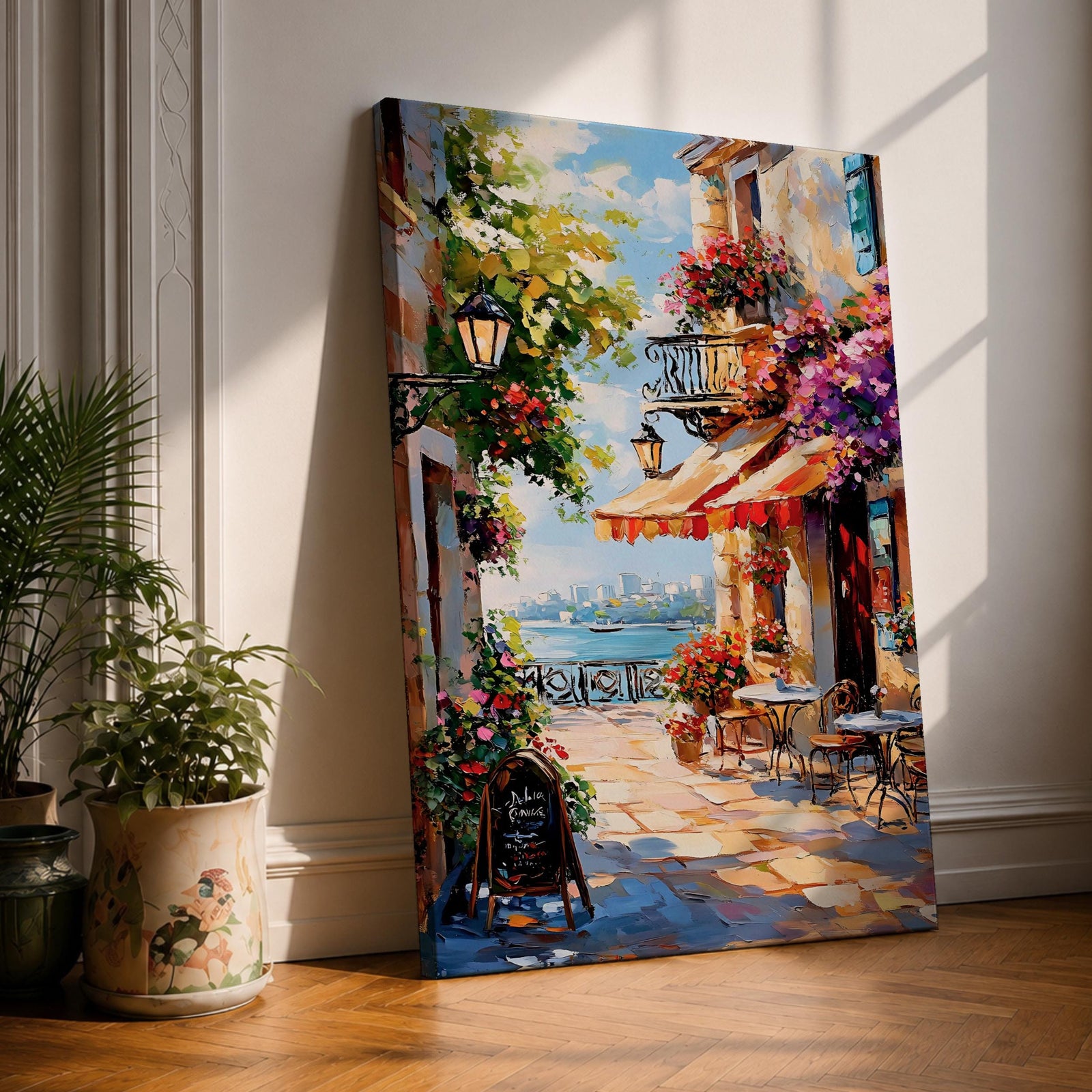A vibrant Mediterranean café scene featuring a cozy outdoor patio with tables and chairs, colorful flowers cascading from balconies, and a distant view of the sea. The artwork captures a lively coastal atmosphere with impressionistic brushstrokes and rich textures, evoking a warm and inviting cityscape.