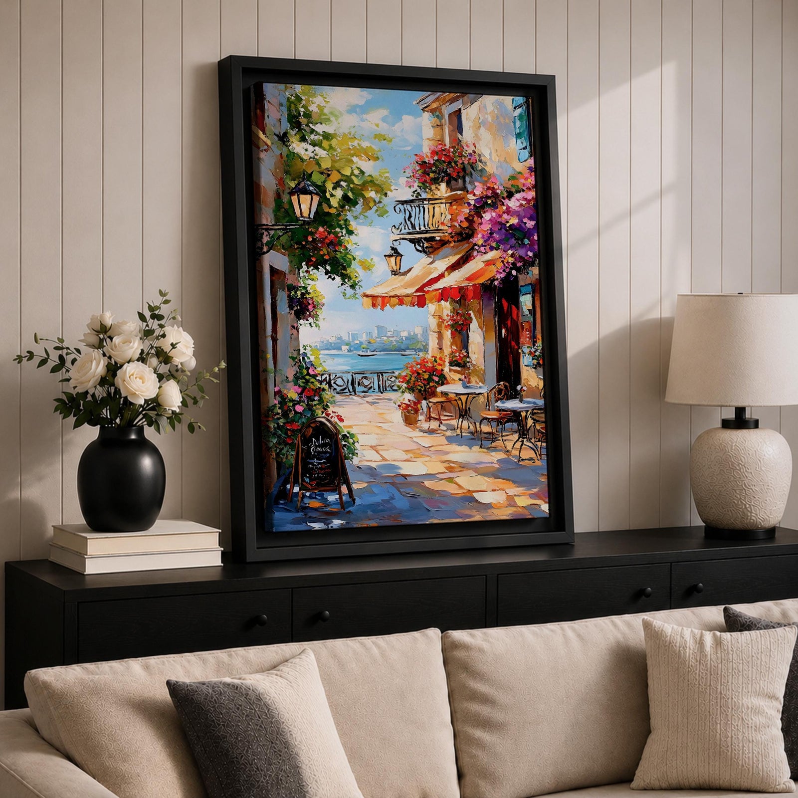 A vibrant Mediterranean café scene featuring a cozy outdoor patio with tables and chairs, colorful flowers cascading from balconies, and a distant view of the sea. The artwork captures a lively coastal atmosphere with impressionistic brushstrokes and rich textures, evoking a warm and inviting cityscape.