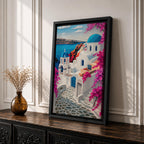 A vibrant framed canvas depicting Santorini, Greece, featuring iconic white buildings with blue domes, winding cobblestone paths, and bright bougainvillea flowers overlooking a deep blue sea, rendered in a clean, graphic style emphasizing architectural shapes and Mediterranean coastal charm.