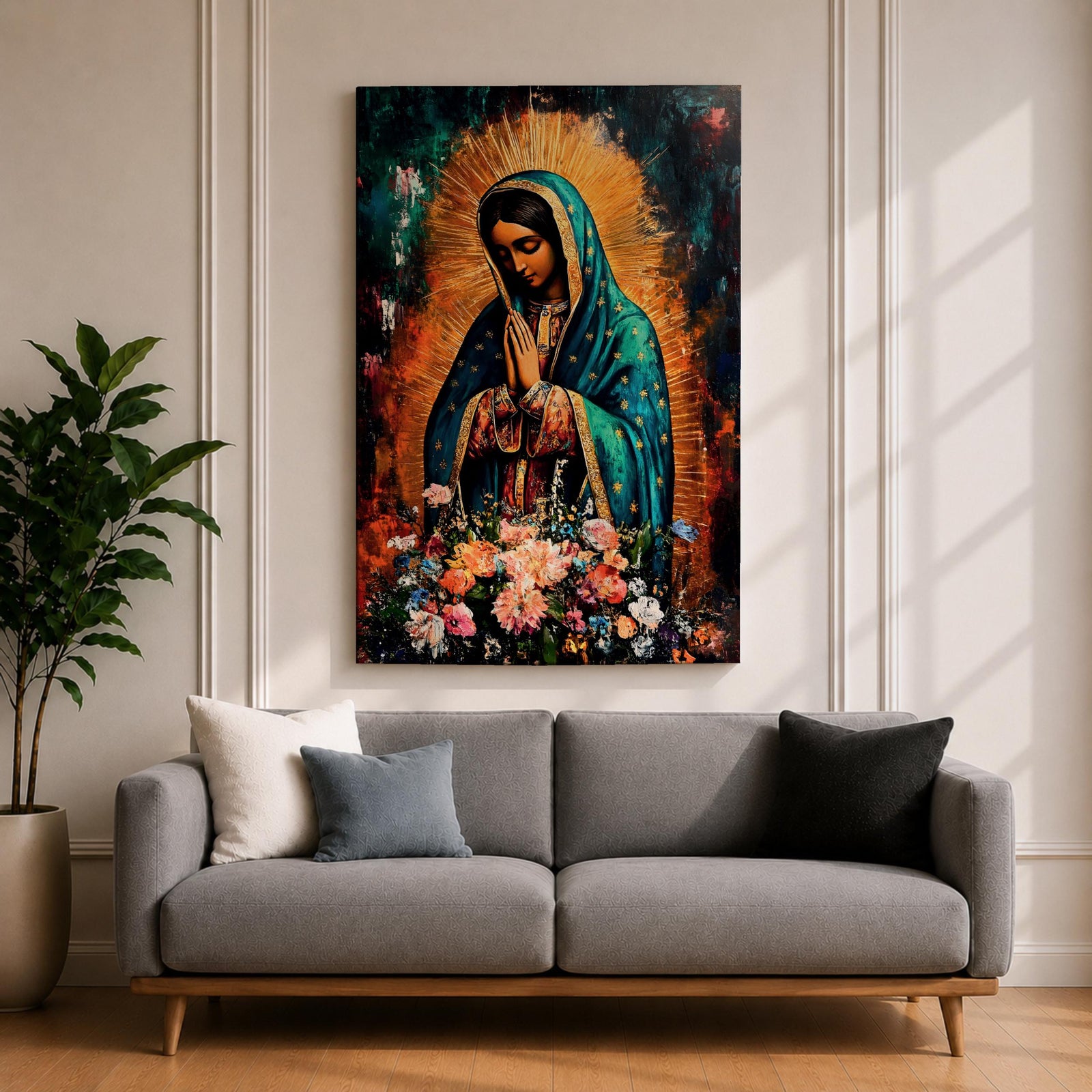 A vibrant framed canvas painting of Our Lady of Guadalupe depicts the Virgin of Guadalupe with hands clasped in prayer, wearing a teal mantle adorned with gold stars and surrounded by radiant light. The foreground features a colorful array of flowers, emphasizing the Catholic religious theme.