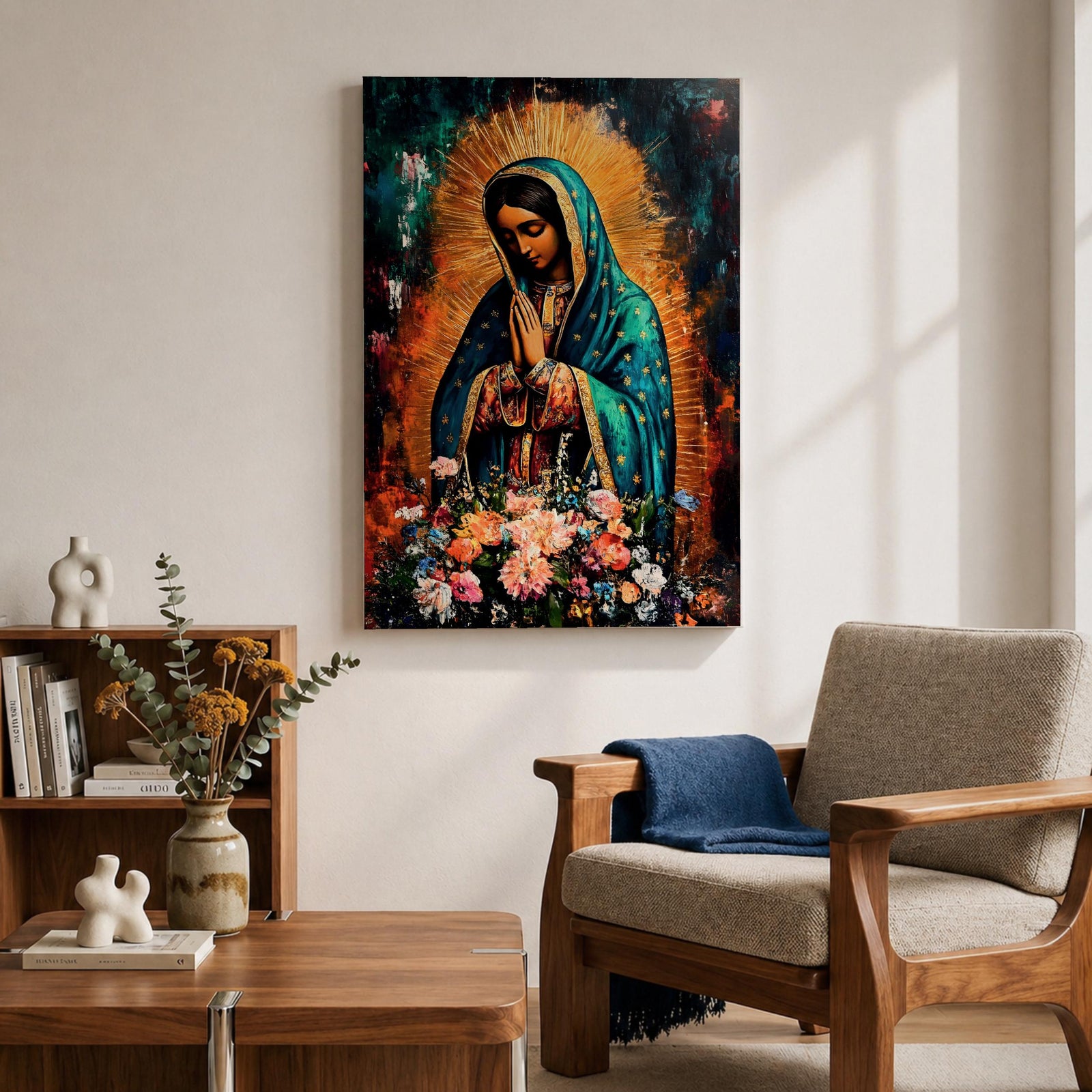 A vibrant framed canvas painting of Our Lady of Guadalupe depicts the Virgin of Guadalupe with hands clasped in prayer, wearing a teal mantle adorned with gold stars and surrounded by radiant light. The foreground features a colorful array of flowers, emphasizing the Catholic religious theme.