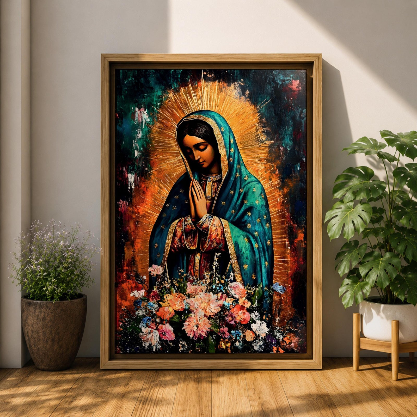 A vibrant framed canvas painting of Our Lady of Guadalupe depicts the Virgin of Guadalupe with hands clasped in prayer, wearing a teal mantle adorned with gold stars and surrounded by radiant light. The foreground features a colorful array of flowers, emphasizing the Catholic religious theme.