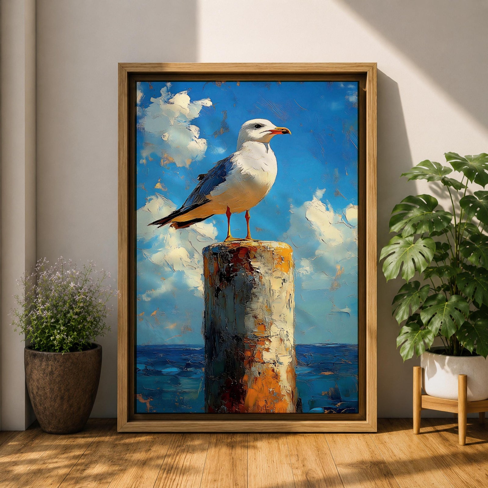 A framed canvas painting of a seagull perched on a weathered post against a bright blue sky with fluffy clouds and a distant ocean horizon. The artwork captures the bird in a realistic style with textured brushstrokes emphasizing the natural coastal scene.