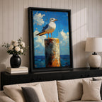 A framed canvas painting of a seagull perched on a weathered post against a bright blue sky with fluffy clouds and a distant ocean horizon. The artwork captures the bird in a realistic style with textured brushstrokes emphasizing the natural coastal scene.
