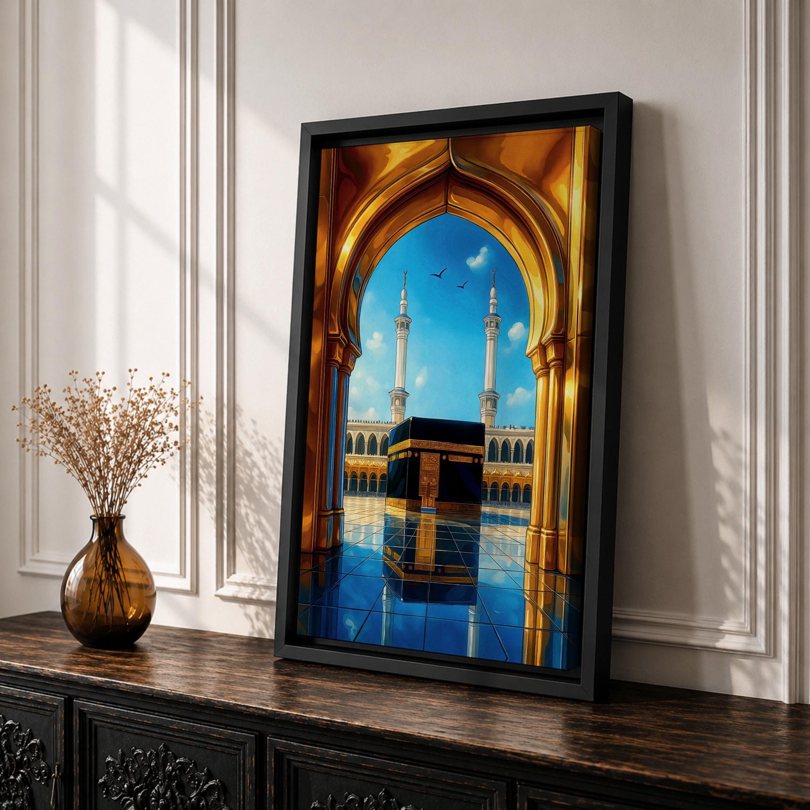 A vibrant framed canvas artwork depicting the Kaaba viewed through a golden arched doorway at Masjid Al Haram in Mecca. The scene shows the iconic black cube structure with gold detailing, two minarets in the background, and a reflective tiled floor under a bright blue sky with birds flying.