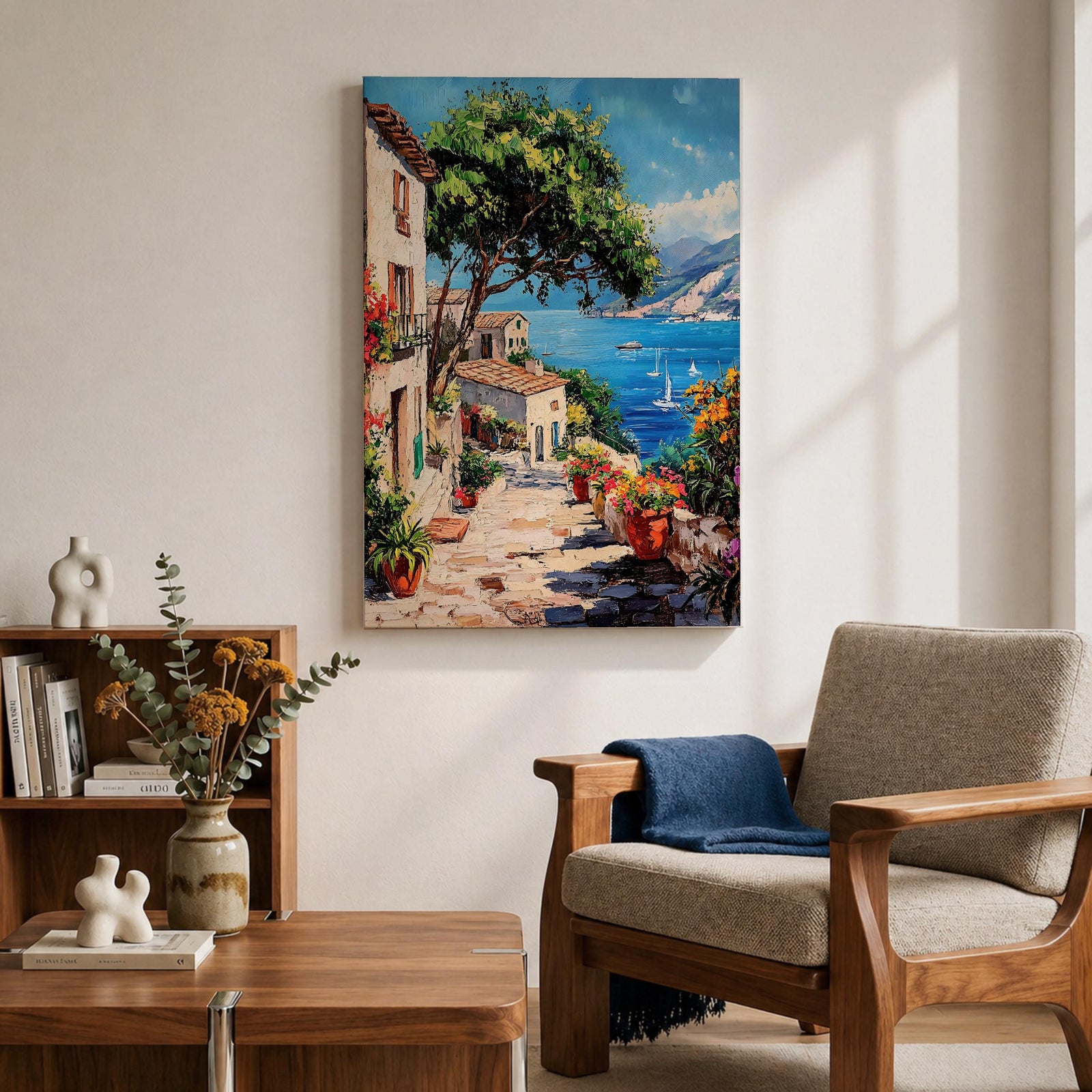 This artwork depicts a vibrant Italian village scene with terracotta-roofed houses, lush greenery, and colorful flowers lining a stone pathway that leads down to a bright blue Mediterranean sea with sailboats and distant mountains, rendered in a realistic style capturing coastal charm.