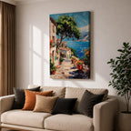 This artwork depicts a vibrant Italian village scene with terracotta-roofed houses, lush greenery, and colorful flowers lining a stone pathway that leads down to a bright blue Mediterranean sea with sailboats and distant mountains, rendered in a realistic style capturing coastal charm.