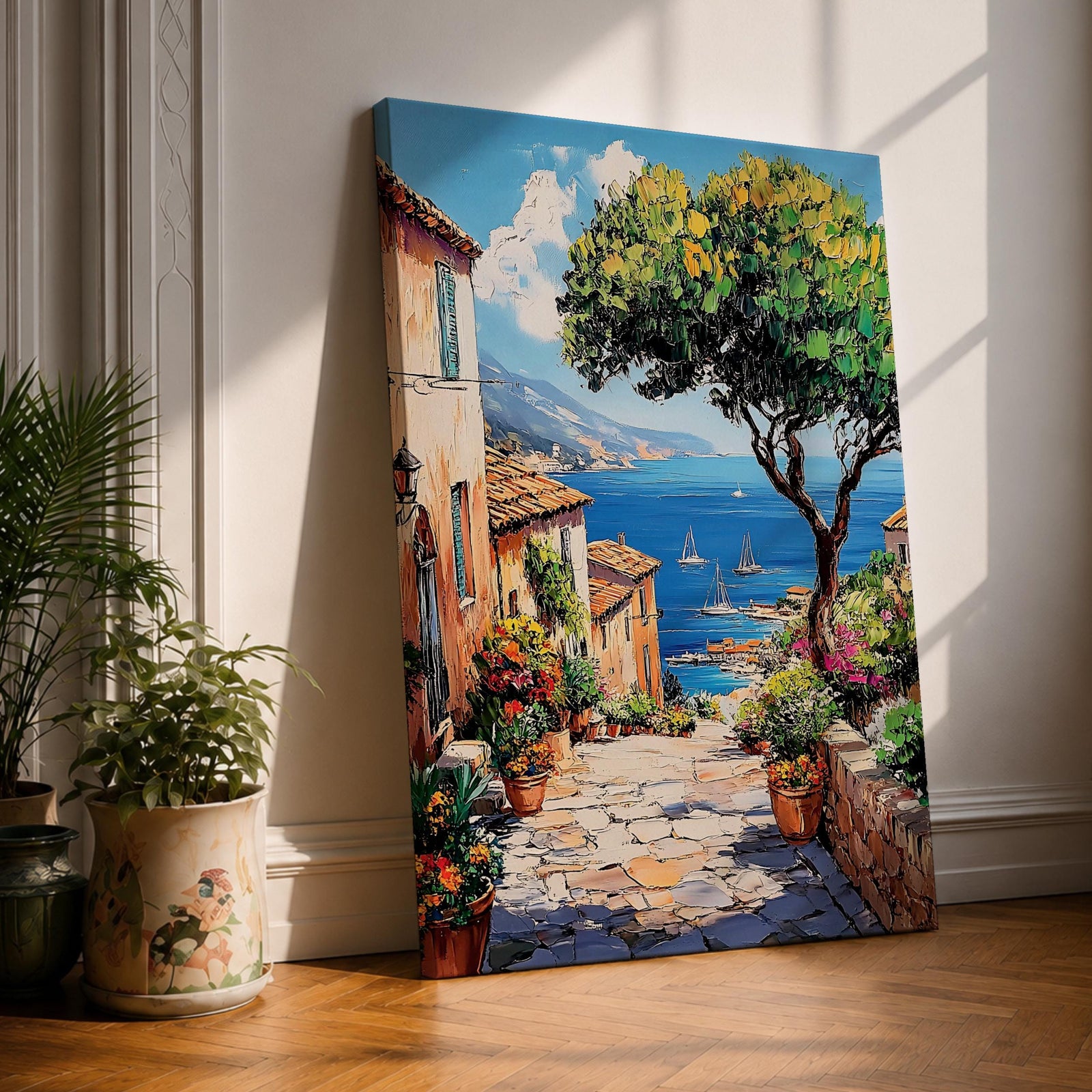 A vibrant framed canvas painting depicting a charming coastal village with stone-paved streets, terracotta rooftops, lush greenery, colorful flowers, and sailboats on a deep blue sea under a clear sky, rendered in a detailed, realistic style capturing Mediterranean summer ambiance.