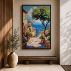A vibrant framed canvas painting depicting a charming coastal village with stone-paved streets, terracotta rooftops, lush greenery, colorful flowers, and sailboats on a deep blue sea under a clear sky, rendered in a detailed, realistic style capturing Mediterranean summer ambiance.