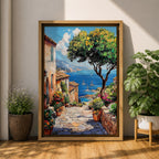 A vibrant framed canvas painting depicting a charming coastal village with stone-paved streets, terracotta rooftops, lush greenery, colorful flowers, and sailboats on a deep blue sea under a clear sky, rendered in a detailed, realistic style capturing Mediterranean summer ambiance.