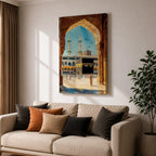 Watercolor style artwork showing the Kaaba at Masjid Al Haram in Mecca framed through a large golden mosque arch, with pilgrims gathered around the courtyard and two tall minarets rising against a clear blue sky.
