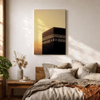 Minimalist artwork of the Kaaba at Masjid Al Haram in Mecca showing the black cubic shrine with gold calligraphy bands against a dramatic golden sunset sky and soft clouds.
