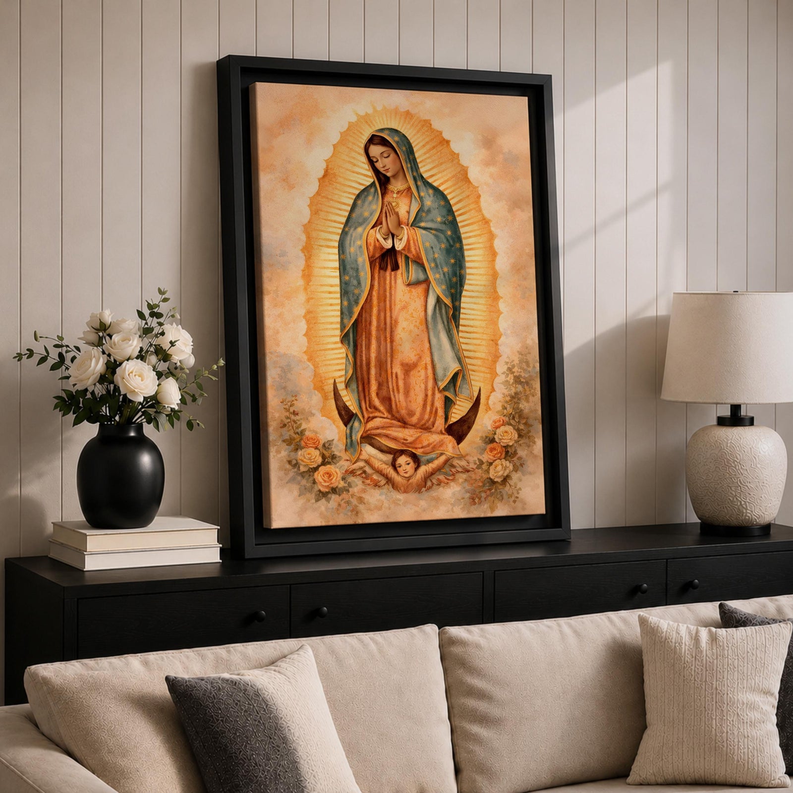Painting of Our Lady of Guadalupe standing in a prayer pose with hands clasped and head bowed, wearing a flowing rose colored gown and a blue mantle decorated with stars, surrounded by radiant golden rays forming an oval halo, standing on a crescent moon supported by a small angel in traditional Catholic devotional style.