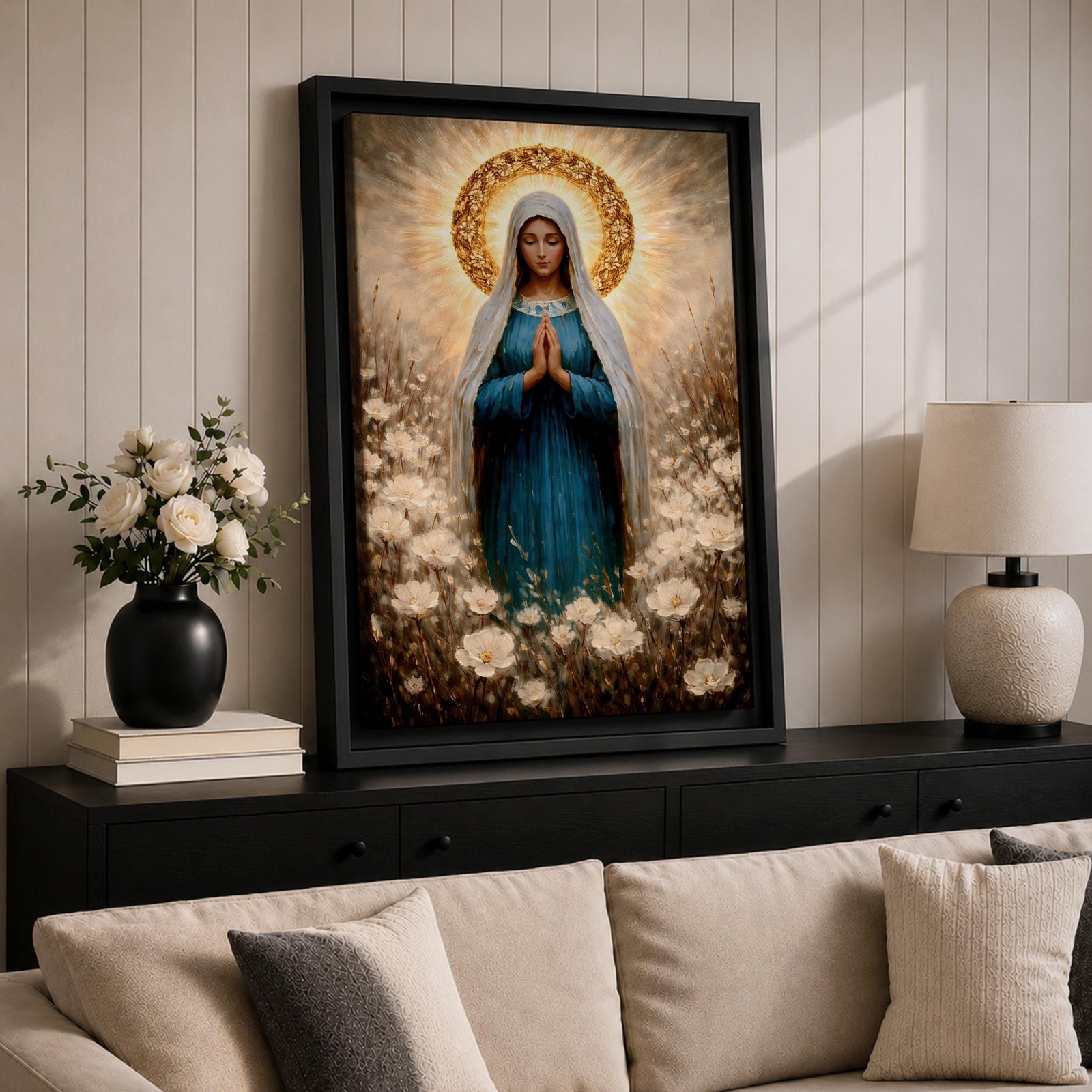 Painting of the Virgin Mary standing in prayer with hands clasped and head bowed, wearing a flowing blue robe and white veil, surrounded by a radiant golden halo and soft glowing light while standing within a field of delicate white wildflowers in a devotional Marian composition.