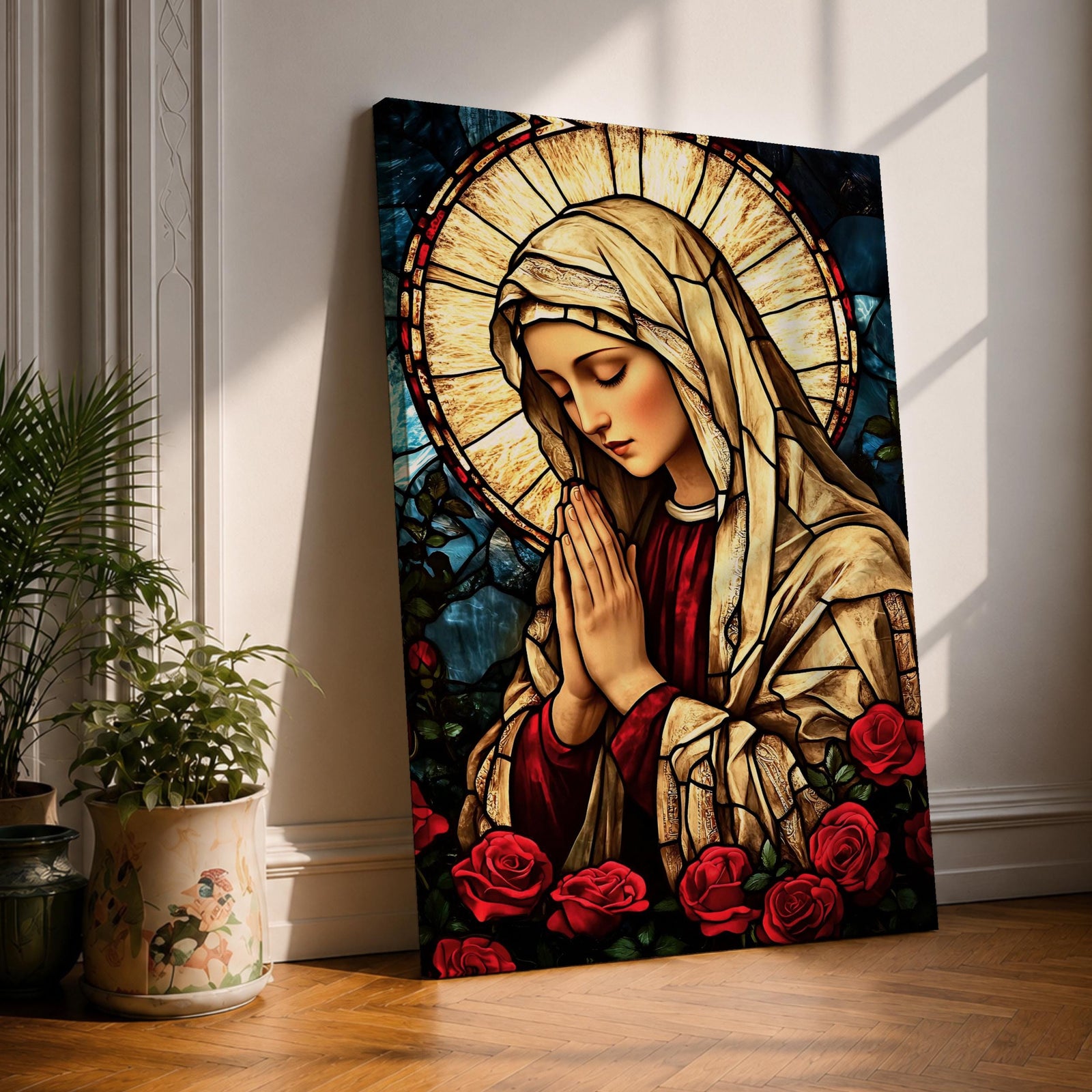 Stained glass style artwork of the Virgin Mary with head bowed and hands clasped in prayer, wearing a cream veil and red garment, surrounded by a radiant circular halo and red roses at the base, rendered with detailed stained glass panels and rich colors in a devotional Marian composition.