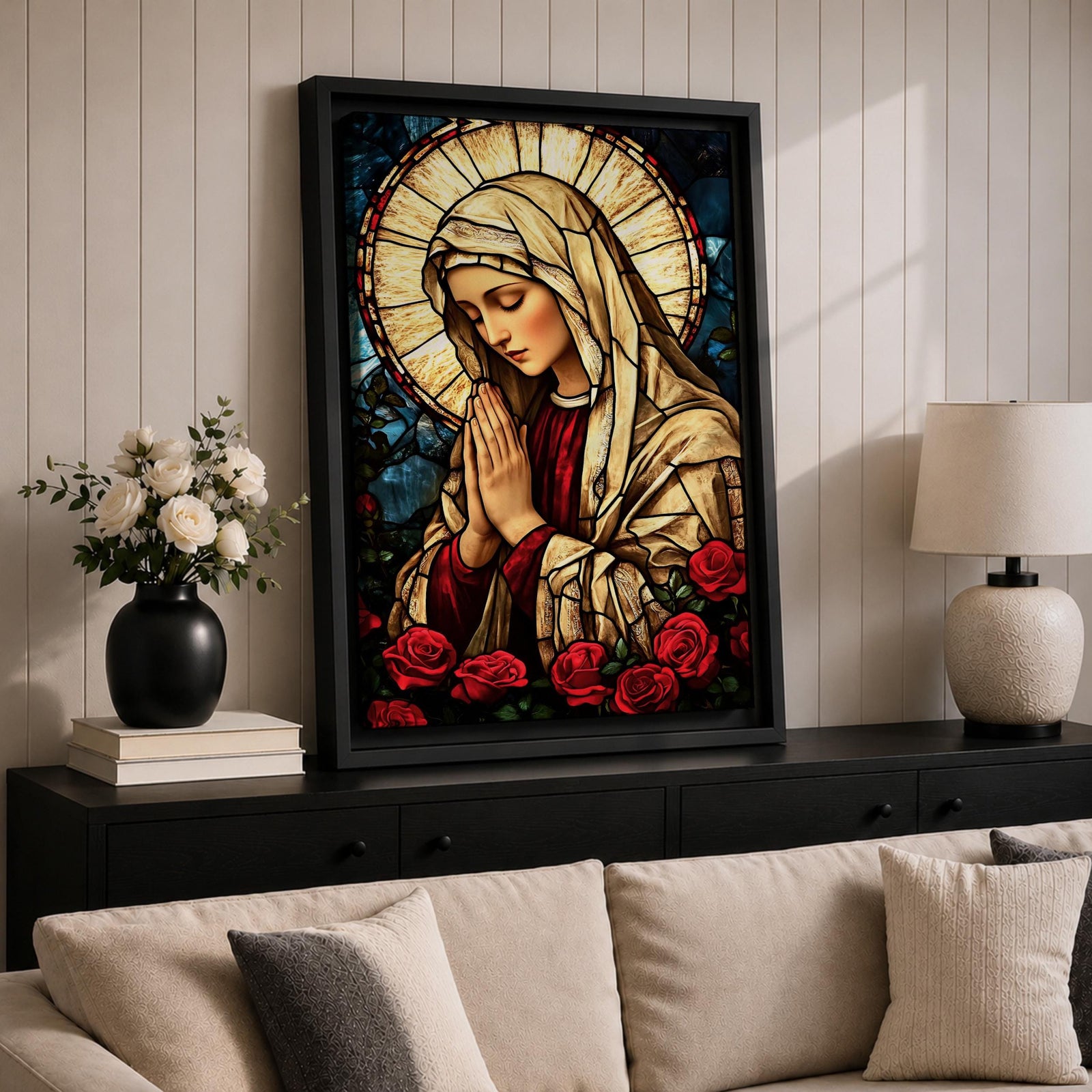 Stained glass style artwork of the Virgin Mary with head bowed and hands clasped in prayer, wearing a cream veil and red garment, surrounded by a radiant circular halo and red roses at the base, rendered with detailed stained glass panels and rich colors in a devotional Marian composition.
