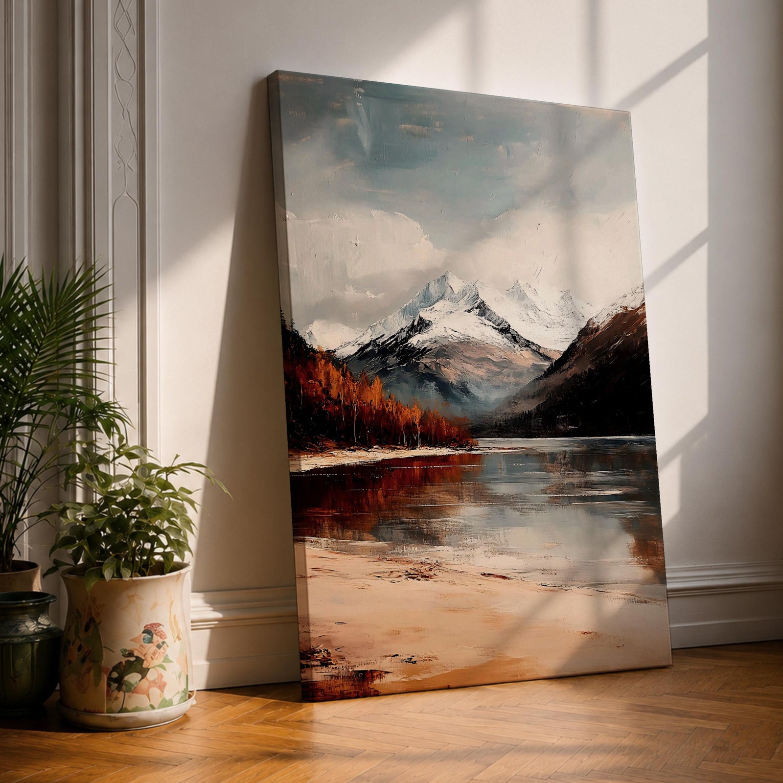 A framed vintage-style painting of a mountain lake featuring snow-capped peaks, autumnal trees, and a reflective water surface, rendered with textured brushstrokes that emphasize a rustic natural landscape.