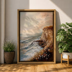 A vintage style framed canvas painting depicting a cliffside ocean seascape with waves crashing against rocky shores and wildflowers in the foreground. The textured brushwork captures the coastal landscape atmosphere with muted tones and a soft sky blending into the horizon.