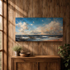 A panoramic seascape painting showing rolling ocean waves moving toward a sandy shoreline beneath a wide sky filled with soft clouds and warm light. The composition stretches across the horizon with textured brushstrokes capturing movement in the water and subtle reflections of blue, white and golden tones across the sea.