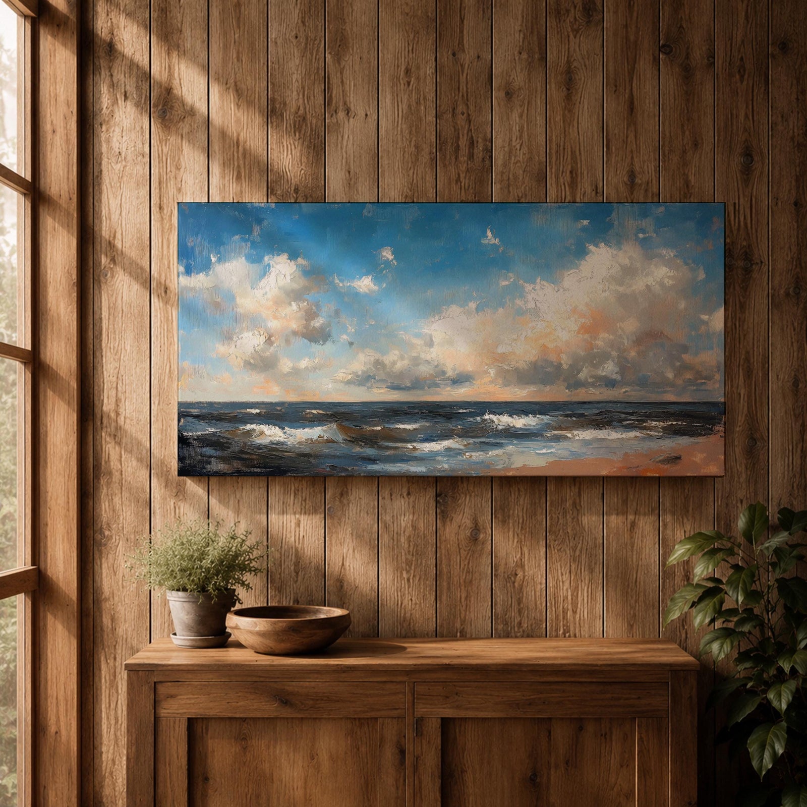 A panoramic seascape painting showing rolling ocean waves moving toward a sandy shoreline beneath a wide sky filled with soft clouds and warm light. The composition stretches across the horizon with textured brushstrokes capturing movement in the water and subtle reflections of blue, white and golden tones across the sea.