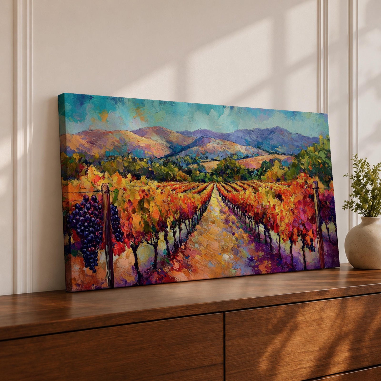 A panoramic vineyard landscape painting showing long rows of grapevines covered in red and golden autumn leaves stretching toward distant mountains beneath a bright sky. Purple grape clusters hang beside the vines while a central path leads through the field, capturing a colorful wine country valley with bold impressionist brushstrokes.