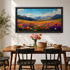 Panoramic painting of a vibrant mountain meadow filled with colorful wildflowers stretching toward distant alpine peaks. Red, yellow, purple, and blue blossoms cover the valley floor beneath a bright sky with soft clouds, while layered mountains rise along the horizon in a luminous natural landscape.