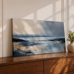 Panoramic abstract coastal seascape painting featuring a calm ocean shoreline with soft blue, gray, and sandy tones reflecting across the water beneath a cloudy horizon.