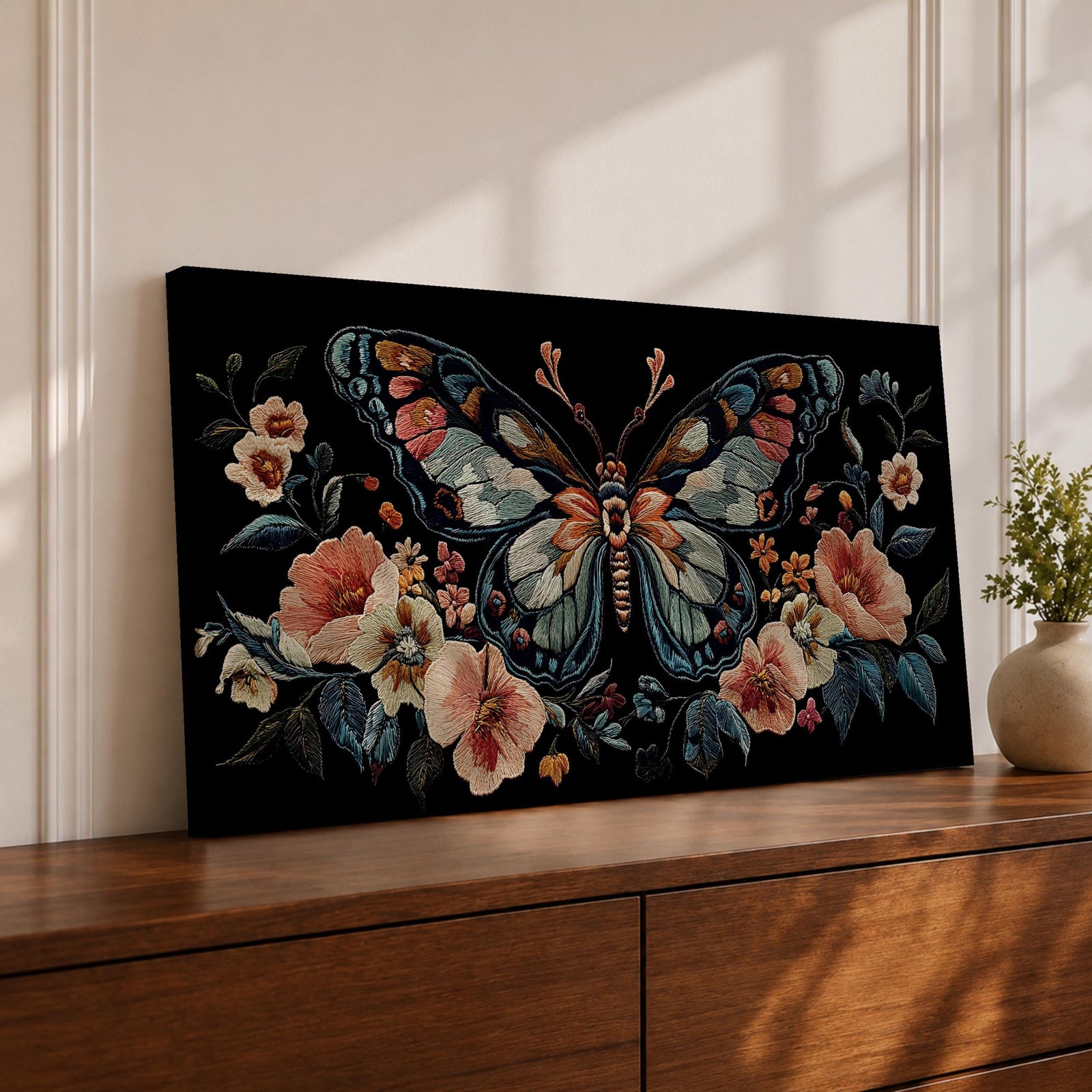 Panoramic artwork depicting a large symmetrical butterfly with intricate patterned wings in blue, cream, and rust tones surrounded by blooming flowers and leafy botanical elements. The composition resembles detailed embroidered textile artwork set against a deep black background with balanced floral arrangements framing the butterfly.