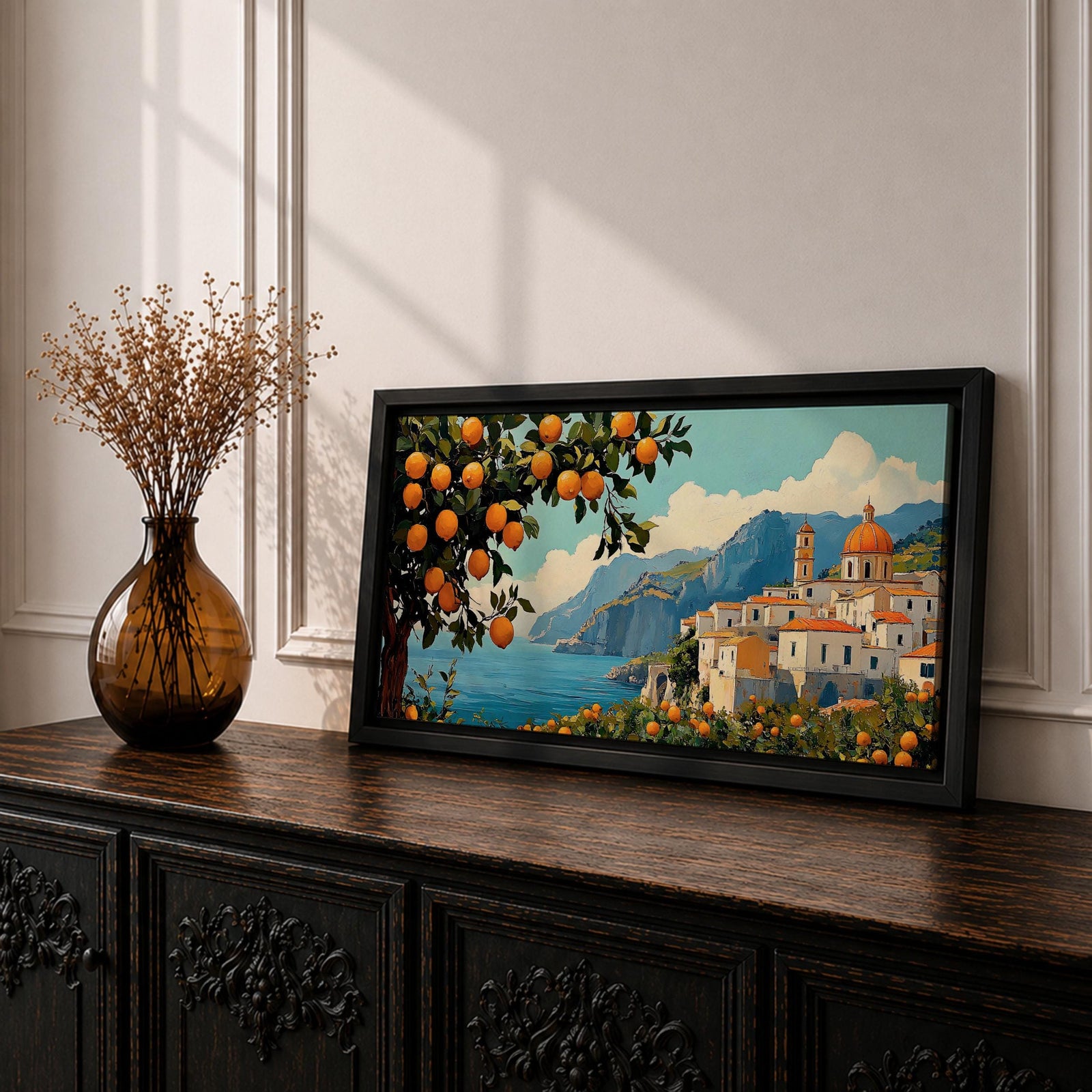 Panoramic coastal artwork showing a Mediterranean village overlooking the sea with white buildings and a domed church set against blue mountains. In the foreground a large lemon tree heavy with bright citrus fruit frames the scene while additional lemons and greenery fill the lower landscape, creating a vibrant Amalfi Coast inspired composition.