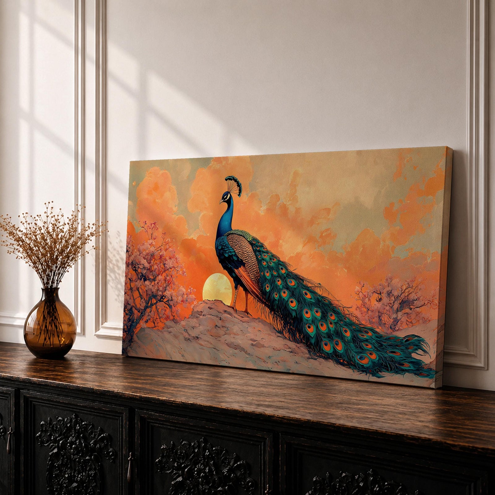 Panoramic artwork depicting a peacock standing on a rocky hill with its long iridescent tail feathers flowing behind it. The bird faces a glowing sunset with warm orange clouds and soft light illuminating the detailed blue and green plumage while flowering trees frame the scene.