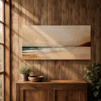 Panoramic coastal landscape painting showing a quiet sandy beach with gentle ocean waves rolling onto the shore beneath a soft sky. Subtle tones of beige, blue, and warm gray create a calm atmosphere while distant hills stretch along the horizon and light reflects across the water.