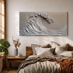 Panoramic textured relief artwork depicting a powerful ocean wave curling upward in sculpted layered forms. The cresting breaker is rendered with thick plaster like ridges and flowing contours in soft neutral tones, creating a minimalist seascape with depth and movement across the wide horizontal composition.