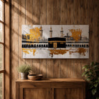 Panoramic painting of the Kaaba in Mecca centered within Masjid al Haram featuring the black cube sanctuary draped in the kiswah with gold calligraphy bands. Tall mosque minarets and long arched colonnades frame the courtyard while bold gold abstract paint textures and layered architectural lines extend across the wide horizontal composition.