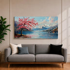 Panoramic painting of a cherry blossom tree in full bloom beside a calm mountain lake with snow covered peaks in the distance and soft clouds above. Pink petals drift across the water while thick palette knife brushstrokes create texture in the blossoms shoreline and reflections forming a wide spring landscape scene with bold color contrast.