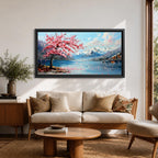 Panoramic painting of a cherry blossom tree in full bloom beside a calm mountain lake with snow covered peaks in the distance and soft clouds above. Pink petals drift across the water while thick palette knife brushstrokes create texture in the blossoms shoreline and reflections forming a wide spring landscape scene with bold color contrast.