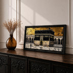 Panoramic gold and black painting of the Kaaba at Masjid al Haram in Mecca, showing the cubed sanctuary draped in the black kiswah with gold calligraphy bands. Surrounding mosque arches and marble courtyard stretch across the horizontal composition while small pilgrim figures circle the Kaaba creating scale and depth.