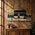 Panoramic gold and black painting of the Kaaba at Masjid al Haram in Mecca, showing the cubed sanctuary draped in the black kiswah with gold calligraphy bands. Surrounding mosque arches and marble courtyard stretch across the horizontal composition while small pilgrim figures circle the Kaaba creating scale and depth.