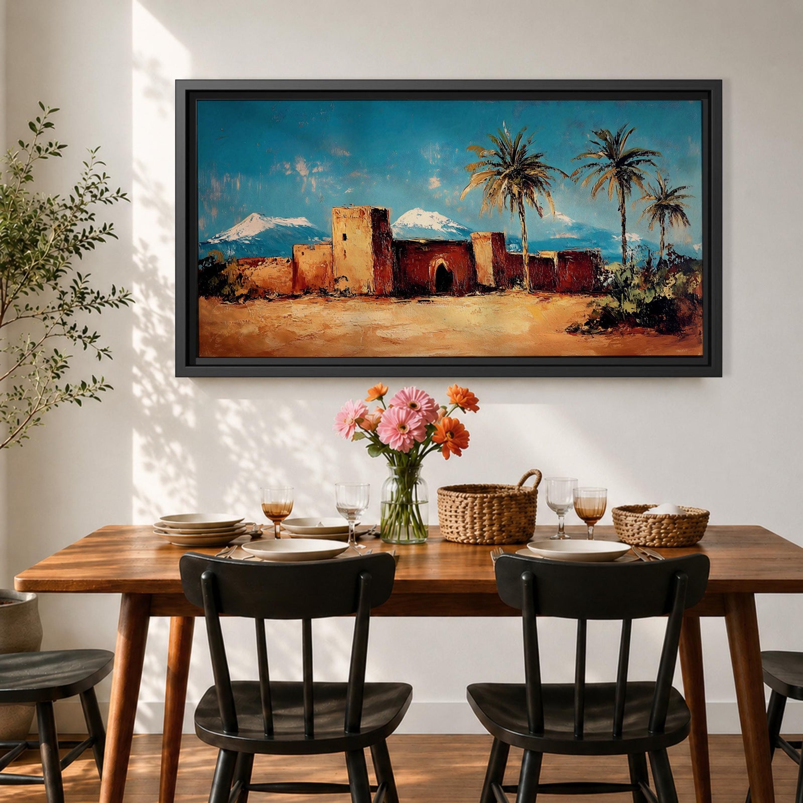 Panoramic painting of a Moroccan kasbah built from warm earthen walls set in a desert landscape with tall palm trees and distant snow capped mountains beneath a bright blue sky. Thick palette knife textures shape the fortress architecture sandy ground and foliage creating a wide horizontal North African landscape scene with bold contrast.
