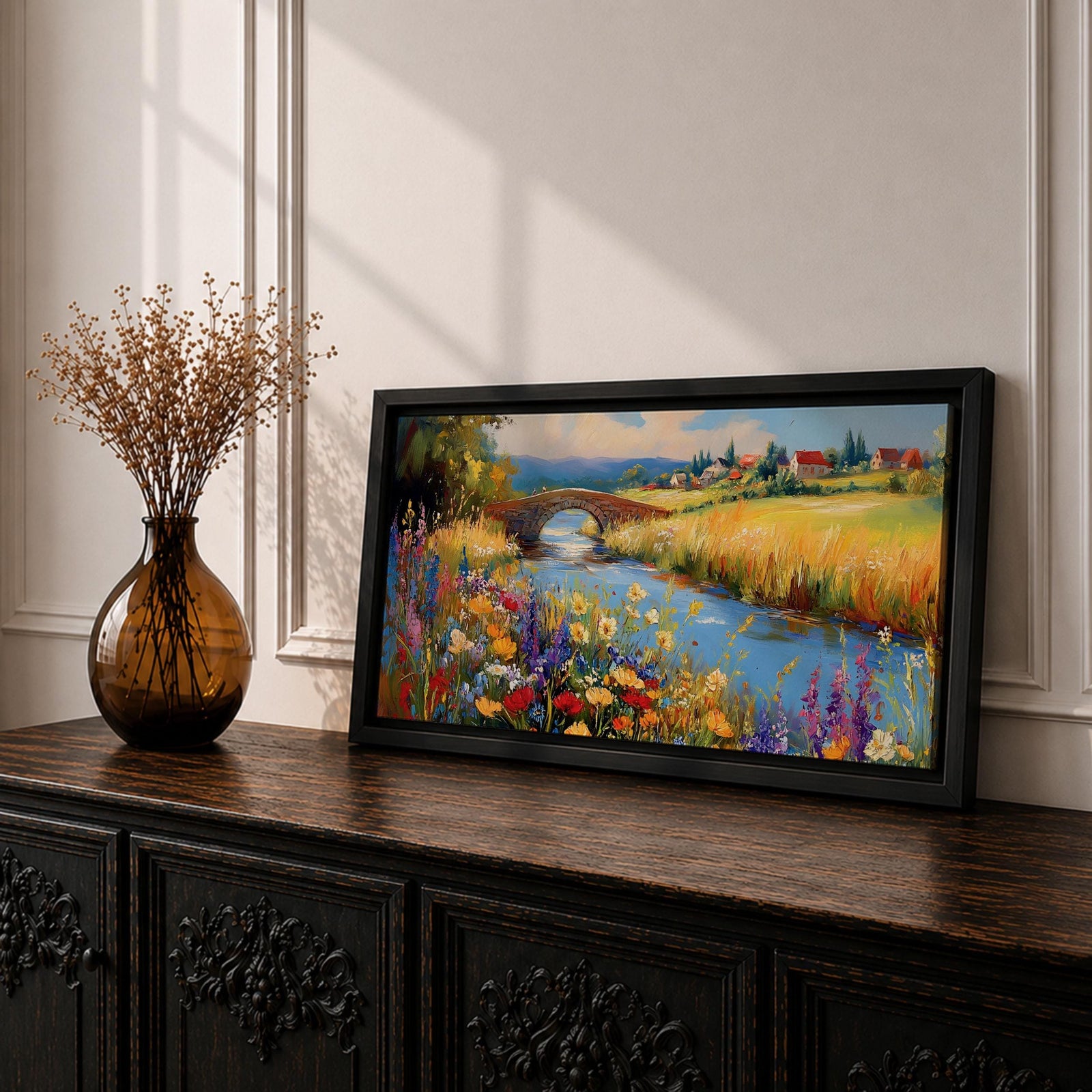 Panoramic landscape painting of a winding river flowing through a countryside meadow filled with colorful wildflowers. A small stone bridge arches over the water while fields, cottages, and rolling hills stretch into the distance under a bright sky, rendered with vibrant textured brushstrokes.