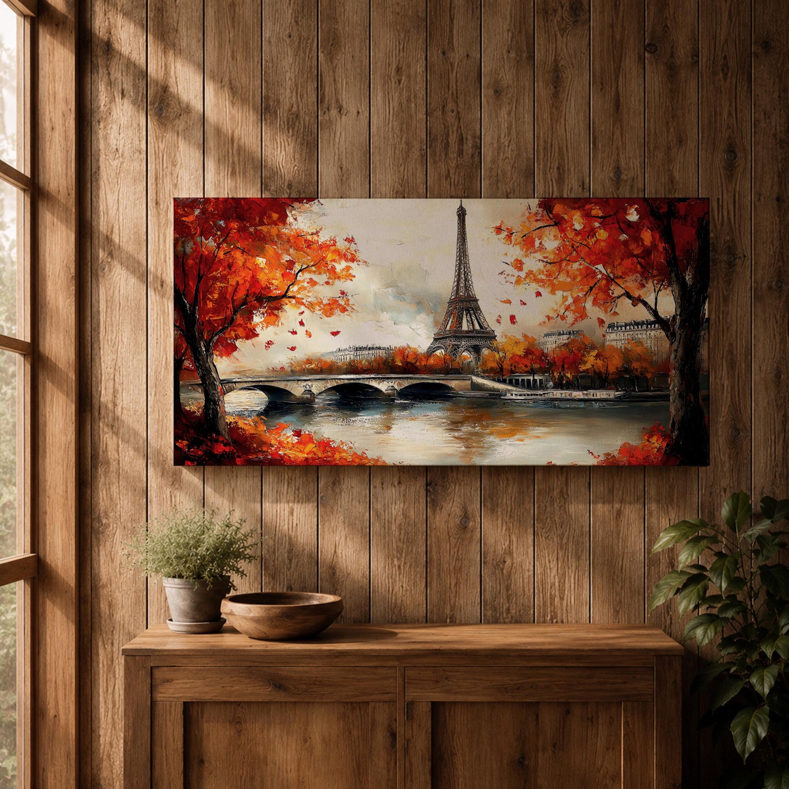 Panoramic painting of the Eiffel Tower rising above the Seine River with an arched stone bridge and classic Parisian buildings along the waterfront. Vibrant red and orange autumn trees frame the scene while textured brushstrokes reflect warm foliage and architecture across the calm river surface.