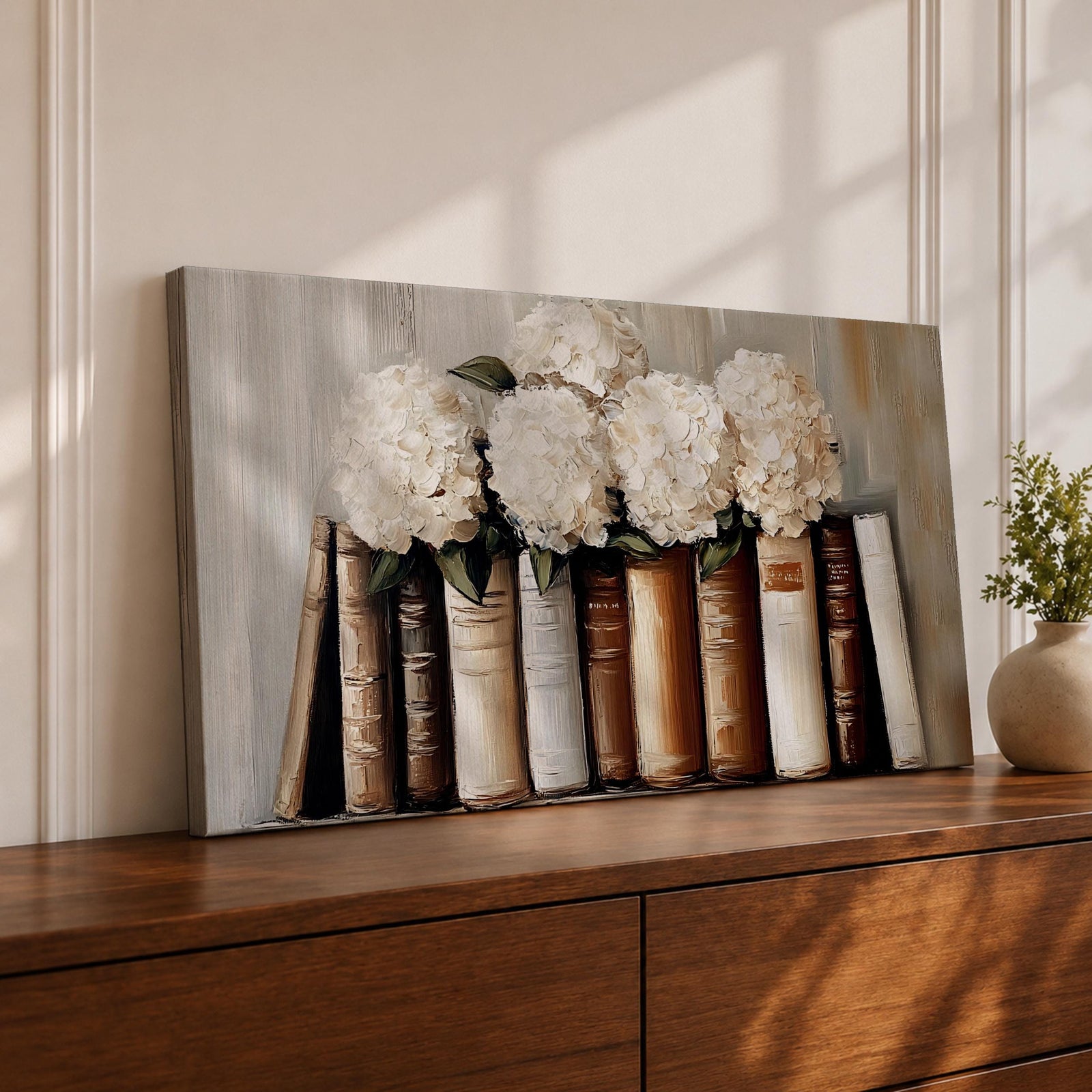 Panoramic still life painting of white hydrangea flowers arranged inside stacked vintage books with neutral beige and cream tones in a soft textured background.