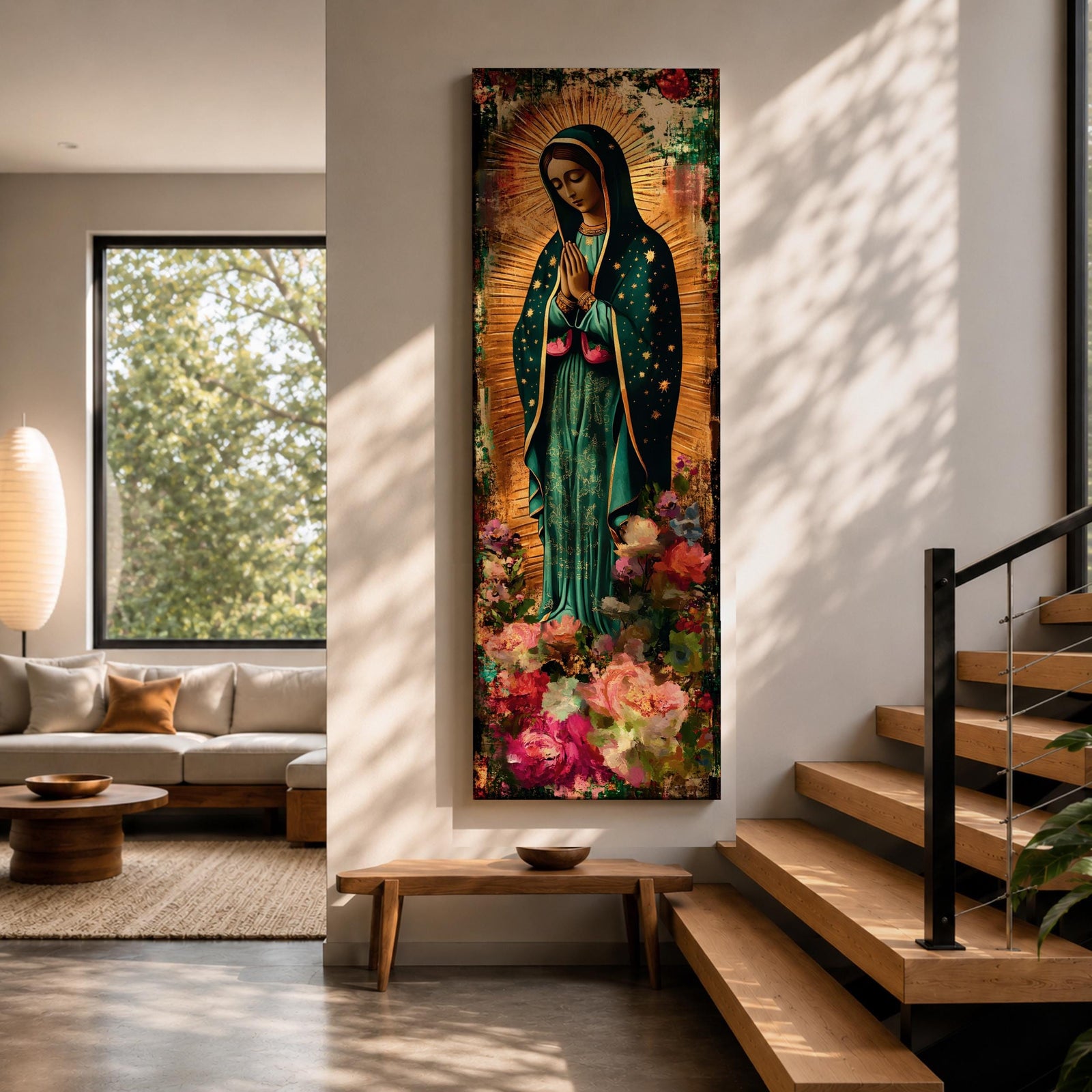 A tall narrow vertical painting of the Virgin Mary Guadalupe shown in prayer with hands clasped, wearing a deep teal mantle adorned with gold stars and a soft pink dress, surrounded by radiant golden rays, with rich floral elements in vibrant pink, red, and cream tones at the base, rendered in a textured painterly style with warm, aged tones.